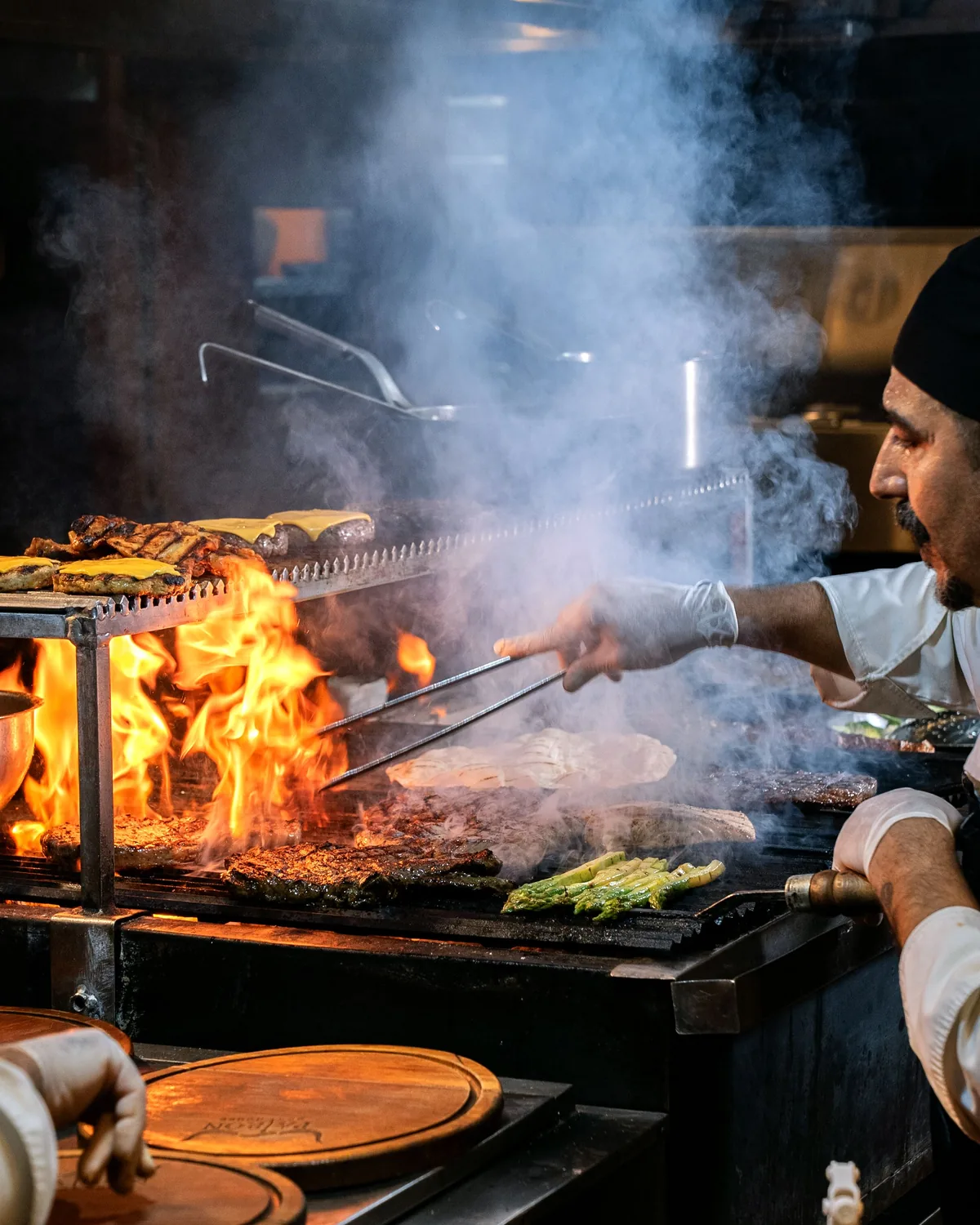A chef grilling meat and vegetables over an open flame at a live cooking station (representative photograph of live-fire cooking)